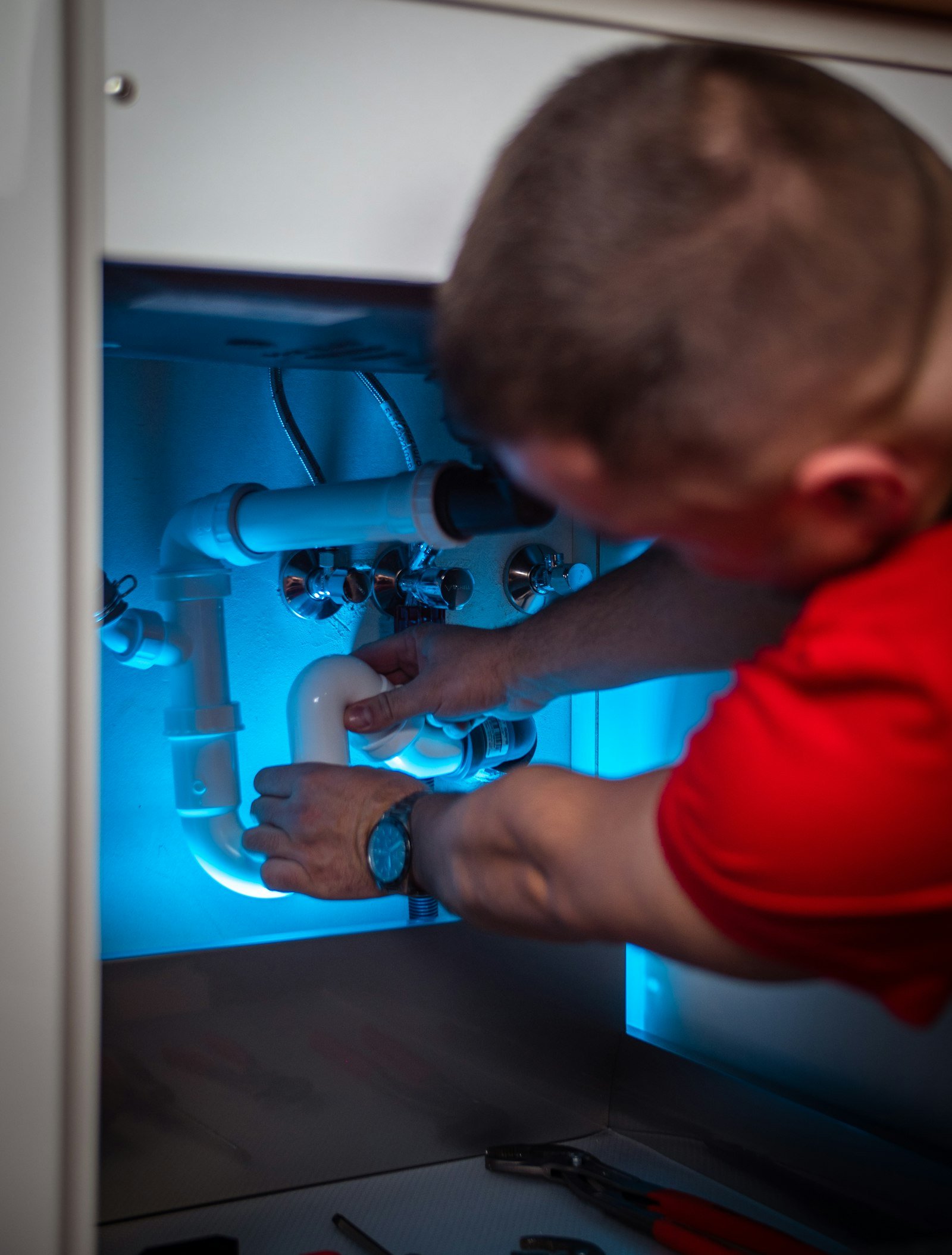 Plumber working on a pipe under a cabinet, representing drain cleaning service in San Antonio TX